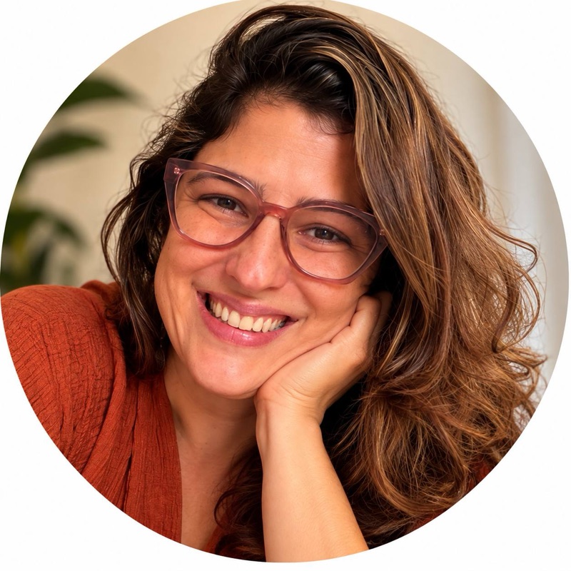 Bia sorrindo, de óculos, com a mão apoiada no rosto.